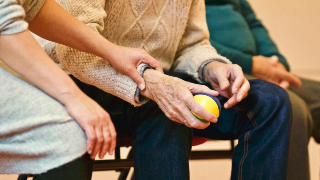 Elderly woman’s frail hand clasped by a care worker’s steady grip—the human cost of the UK care worker visa crackdown.